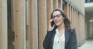 Attractive business woman with eye glasses smiling portrait. Young business people confident pretty. Female goes with smartphone in the city. Growing, success. 4K slow motion video
