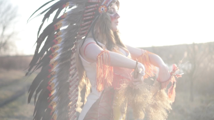 Beautiful girl in native American Indian headdress and costume with colorful make-up turning in the rituale dance. Close-up of her face. Royalty-Free Stock Footage #1039392224
