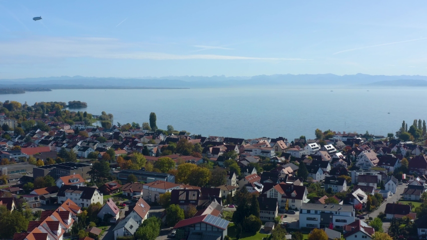  Aerial view of the city Immenstaad beside the lake Constance in Germany on a sunny day in autumn, fall. Descend beside the town with blimp in the back.