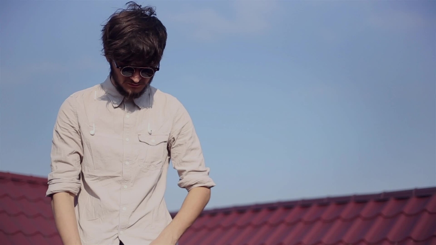 Portrait of hipster with round sunglasses on red roof, background of sky.