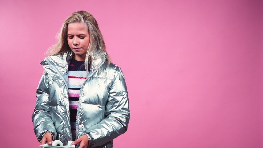 Medium Lockdown Shot Of Blond Teenage Girl Putting On Headphones And Dancing Against Pink Background