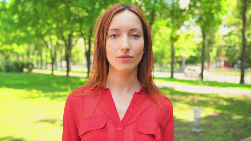 happy caucasian girl showing thumb up hand gesture cheerful female in red shirt standing on the street nature summer background