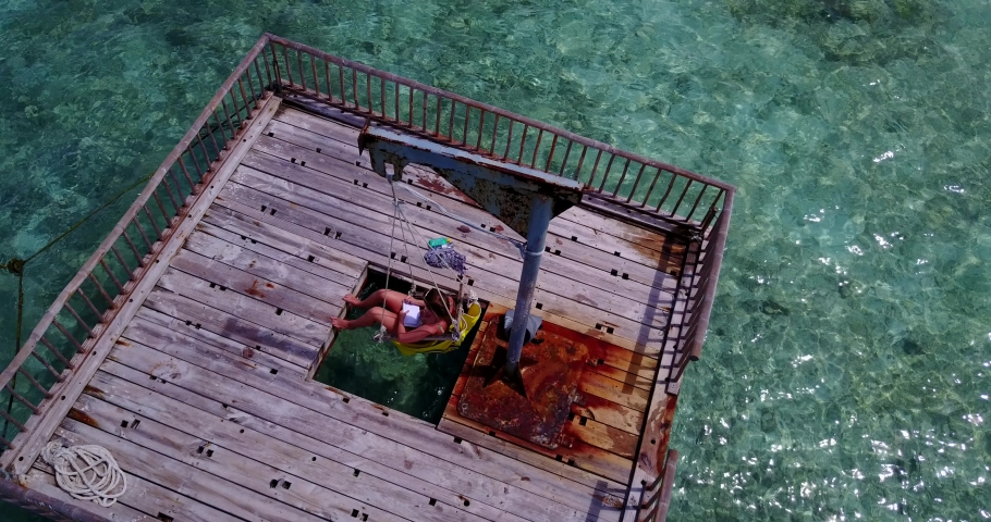 Top view of a young woman sitting at a yellow swing, relaxing on swimming platform in Diwaran, Philippines