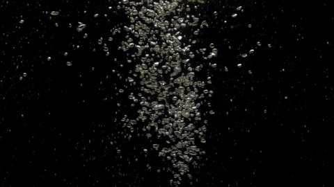 Numerous small air bubbles rise up under crystal clear water, mixing and rise up, swirling softly underwater on the black background with copy space. Underwater bubbles mayhem. Slow motion. Close-up