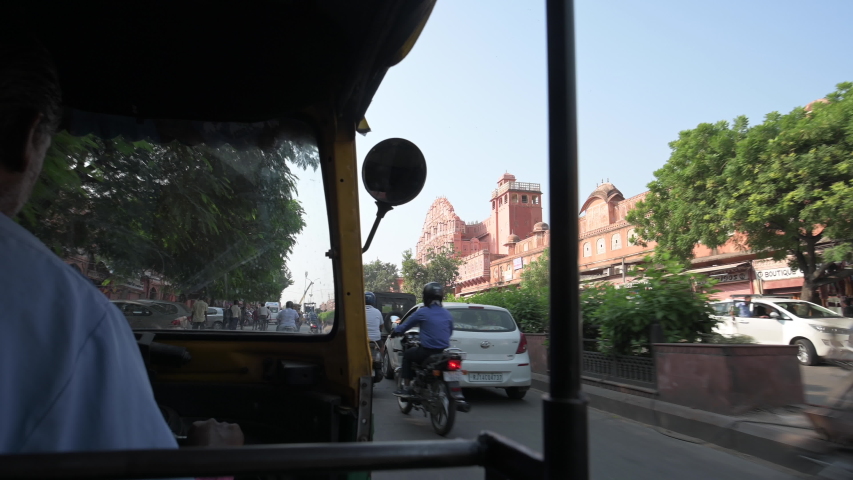 A unidentified driver is riding his auto rickshaw (also known as Tuc Tuc) through the busy streets of the pink city of Jaipur. Beautiful Hawa Mahal in the background. 