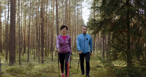 MED TRACKING Middle aged Caucasian couple or friends practicing nordic walking on a scenic forest trail in autumn. 4K UHD 50 FPS SLOW MOTION RAW graded footage