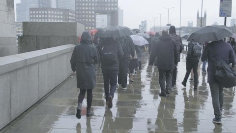 LONDON / UNITED KINGDOM  - OCTOBER 2019 : Commuters walking in the rain at rush hour on London Bridge, London