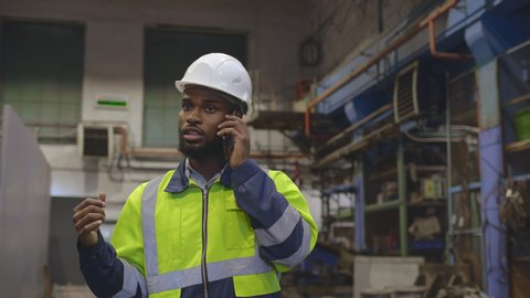 A portrait of an industrial afro-american man engineer with smartphone in a factory, working