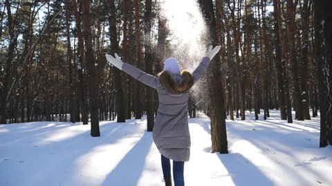 Unrecognizable woman running through snowy forest and throwing handful of snow. Cheerful girl enjoying beautiful winter day. Carefree lady having joyful emotions outdoor. Winter concept. Slow motion