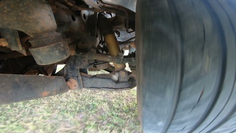 Close up of a car tire with suspension system while moving on grass in countryside