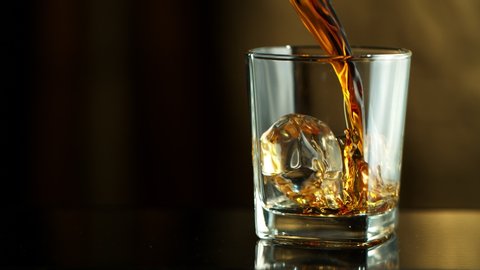 Super Slow Motion Macro Shot of Pouring Whiskey into Glass with Ice Cubes at 1000fps.