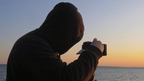 Hoodie wearing photographer takes photos of sun rise over the Black Sea in Odessa Ukraine