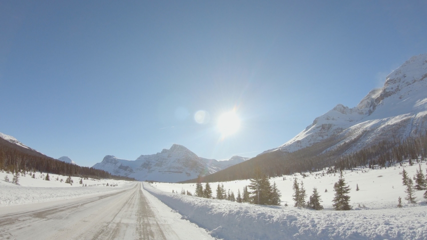 Point of view from drive's side, vehicle driving on snowy mountain road. Car drive along stunning scenic road in winter on a sunny day. Shot from outside the windshield. Royalty-Free Stock Footage #1039441502