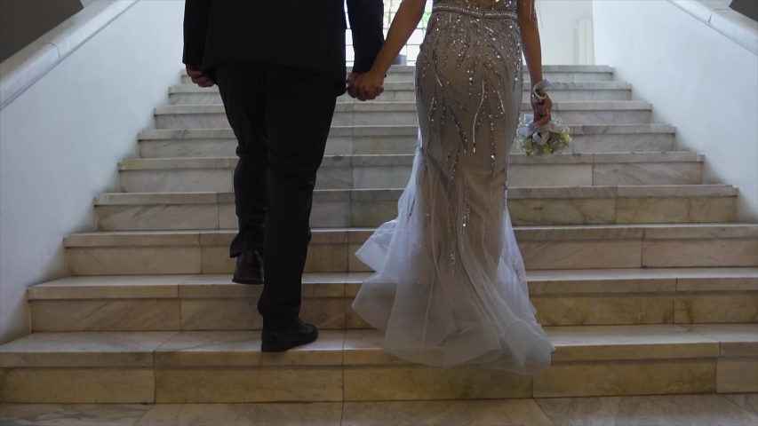 A loving couple holds hands and climbs the stairs to a beautiful white museum.