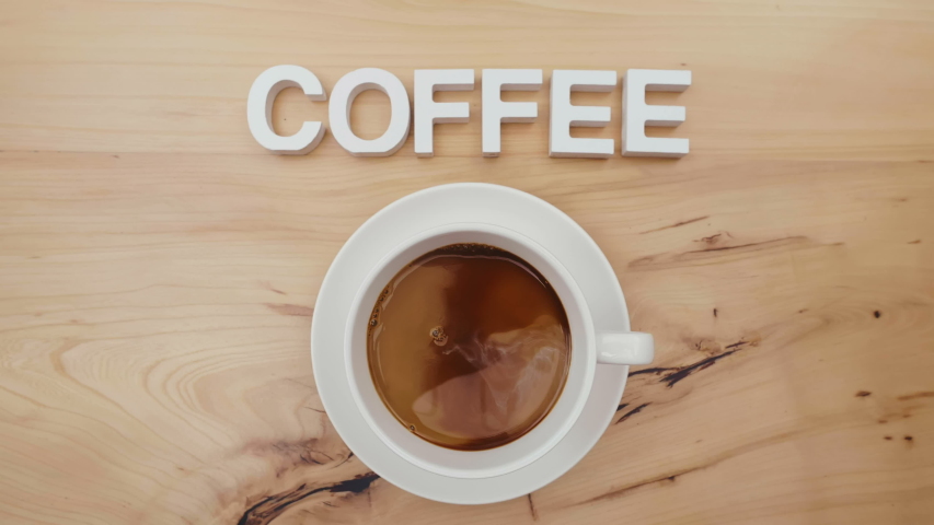 Close up male hand stirs coffee with milk in white cup takes cup in order to try beverage. Word coffee is written above