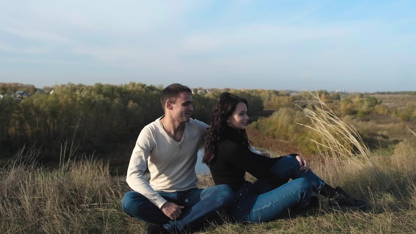 romantic couple sitting on the edge of a cliff. The river flows below. Autumn season. A man and a woman hug and laugh. happy lovers on the background of the river and yellow autumn forest.