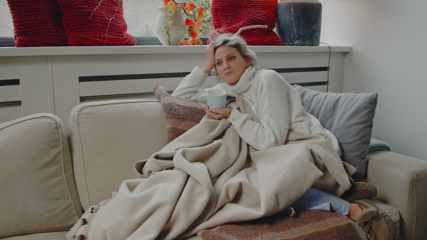 Young caucasian woman on a comfortable couch drinking a cup of hot tea or coffee while being carefree and happy thinking about good memories