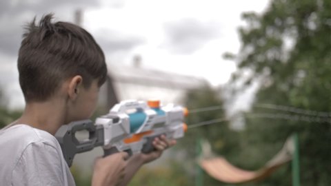 happy boy shoots a water pistol outdoors, have fun