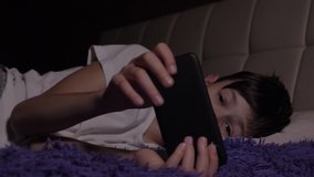 funny boy uses the phone and lying on the bed in the evening