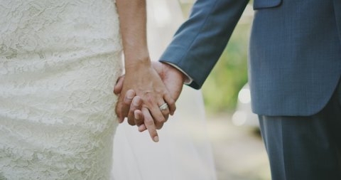 Close up shot of a bride and grooms hands interlocked showing a diamond ring, close up of couple holding hands on their wedding day walking together down the aisle