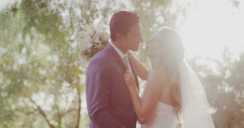 Happy young diverse couple kissing on their wedding day in nature with a backlit sun flare, amazing marriage moments in nature