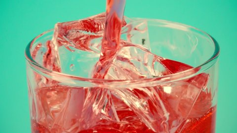 Pouring red soft drink into a glass full of ice cubes against cyan background, close-up slow motion shot on Red