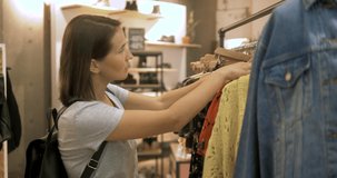 shopping, fashion, style and people concept - happy woman choosing clothes in shopping mall or clothing store