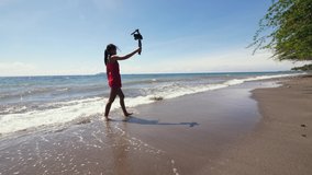Travel woman vlogger walking on the beach and recording vlog on DSLR camera.
