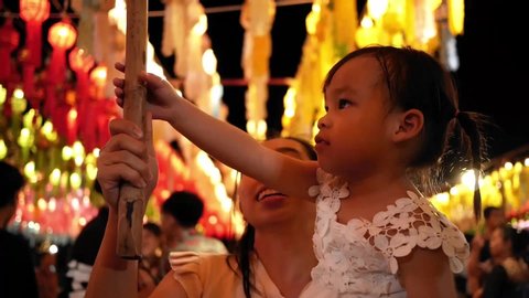 Happy Asian family hanging a thai lanna lantern to make a wish in Yi Peng Festival at the Cham Devi courtyard, Lamphun province. 