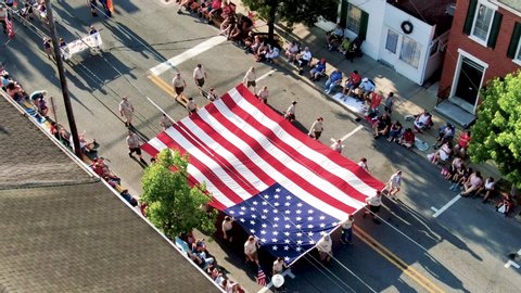 Lititz , PA / United States - 07 04 2019: Tilt down pan aerial shot of Boy Scouts of America carrying start spangled banner American flag in small town parade