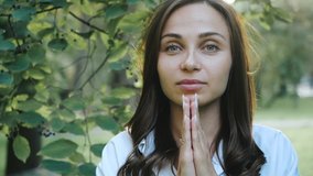 Girl prays to God in christian or catholic religion. Woman folded her hands and closed eyes in prayer in faith. Slow motion video portrait of believing student praying for peace.