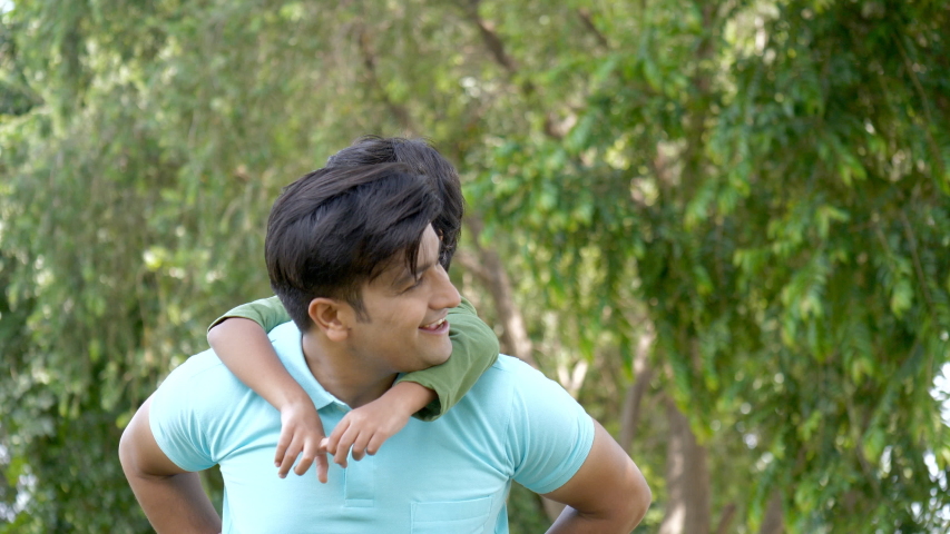 Indian father and son enjoying the weekend while playing in a park - happy family. Happy little boy having a fun ride on his daddy's back on a beautiful summer day - fatherhood concept Royalty-Free Stock Footage #1039499546