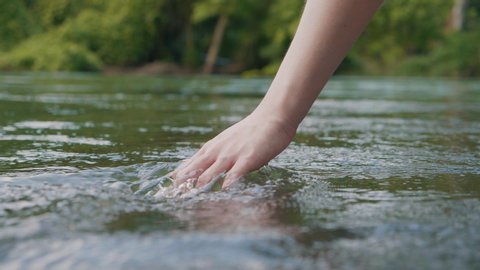close up woman hand gently touches the surface of the water in the forest river or lake