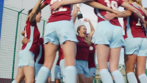 Soccer team of young women jumping all around captain who holding Cup and feeling happy because of win