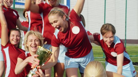 Happy women in soccer sportswear getting Cup, celebrating win and hugging each other