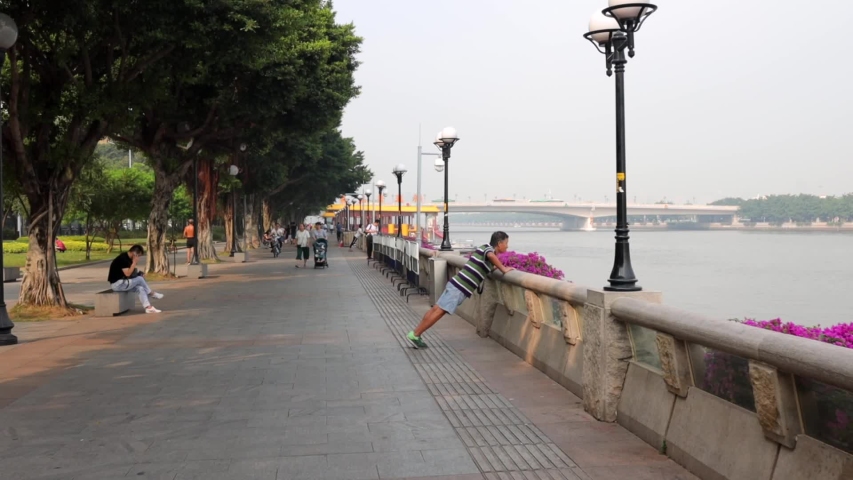 Guangzhou, China - OCT 21 2019: Chinese man goes in for sports on the waterfront. People walk around, mopeds ride