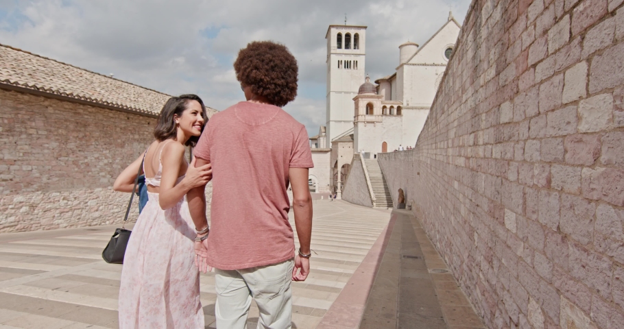 Romantic couple walking feeling free and happy to the main square in rural town of Assisi.Medium shot.Friends italian trip in Umbria.4k slow motion