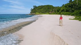 Drone aerial follows young woman walking on the paradise Anse Bazarca beach. Aerial 4k footage view of tanned girl on beautiful Mahe island. Travel concept
