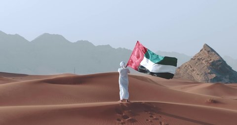 Emirati Holding UAE flag walking on desert dunes celebrating the n ational day - Flag Day 2nd December. 