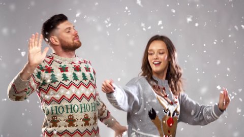 celebration, fun and holidays concept - happy couple wearing knitted sweaters dancing at christmas party