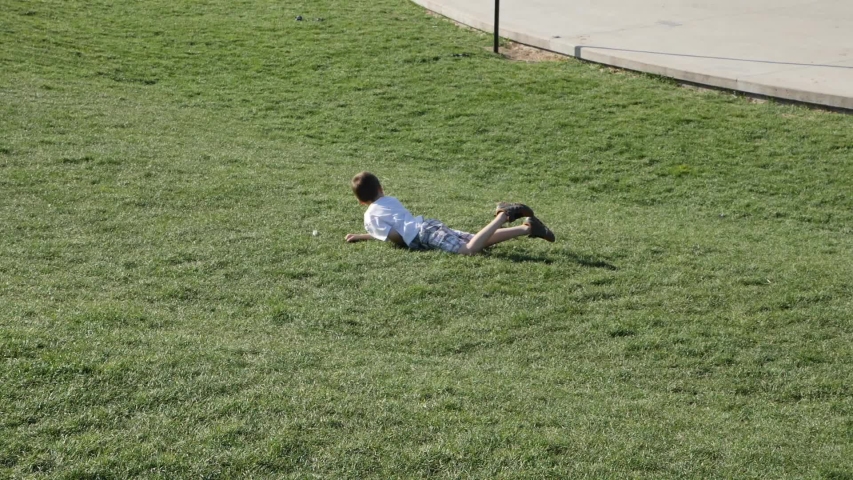 Children roll and summersault down a grassy hill in the park