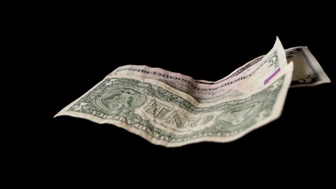 Dollar bills are blown away in front of a black background