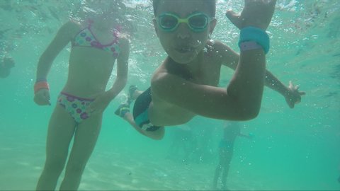Boy in swimming goggles dives and swims underwater. Camera rotating after boy swirling under water