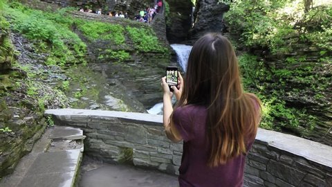 Young female tourist takes photo of waterfall on mobile phone slow motion gimbal