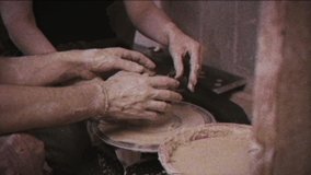 Vintage effect. A potter teaches a woman to make clay dishes. Glitch. Family video archive. Retro. A man takes a woman's hands. Ceramist makes a jug of clay on a potter's wheel. Family business. Help