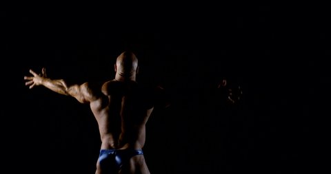Body brutal bald muscular male bodybuilder closeup on black background, he poses, shows muscles. The view from the back.