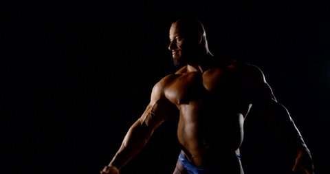 Body brutal bald bearded muscular male bodybuilder closeup on black background, he poses, shows muscles.
