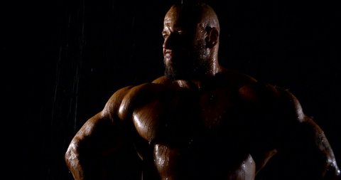 Portrait of a brutal muscular bald bearded male bodybuilder close-up on a black background, he poses.