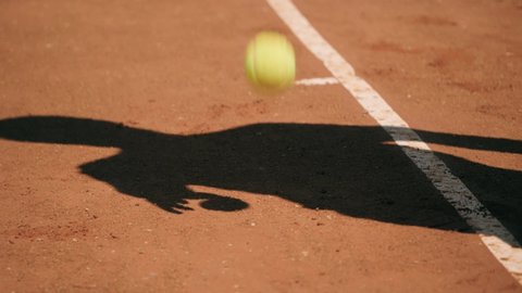 Shadow of tennis player bouncing ball on clay court and serving.