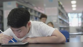 Asian preteens boys using tablet computer at library . Two boy drawing on tablet computer with smile face.